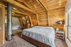 Carpeted bedroom featuring wooden walls, wooden ceiling, and lofted ceiling with beams