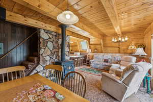Living area featuring wooden walls, a wooden ceiling with exposed beams, a wood stove, and a chandelier