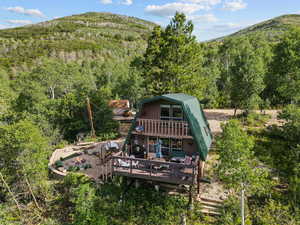 Back of property with a gambrel roof, a view of trees, an outdoor fire pit, a deck with mountain view, and a balcony