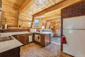 Kitchen featuring white appliances, a wood ceiling with exposed beams, light countertops, a peninsula, and wooden walls