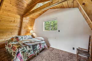 Carpeted bedroom featuring a wooden ceiling with exposed beams and wood walls