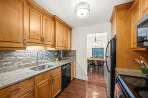 Kitchen featuring light granite counters, dark wood-type flooring, stainless and black appliances, decorative backsplash, and wood finish cabinetry