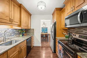 Kitchen with over sink lighting, stone countertops, tasteful backsplash, dark wood-type flooring, and new light fixture