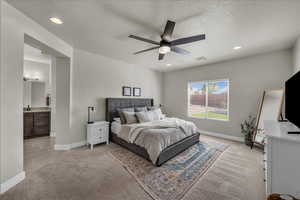 Bedroom with light colored carpet, a ceiling fan, a textured ceiling, ensuite bath, and recessed lighting