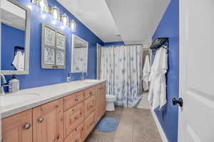 Full bathroom featuring double vanity, a textured ceiling, light tile patterned floors, and shower / tub combo