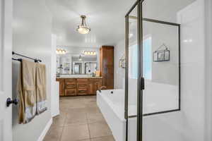 Primary Bathroom featuring double vanity, light tile patterned flooring, a garden tub, and a stall shower