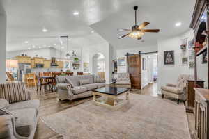 Living room with a barn door, arched walkways, light wood-type flooring, vaulted ceiling, and ceiling fan