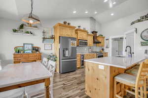 Kitchen featuring light wood finish cabinets, stainless steel appliances, decorative backsplash, a center island with sink, and a breakfast bar area