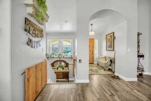 Hallway with arched walkways, light wood-style flooring, and lofted ceiling