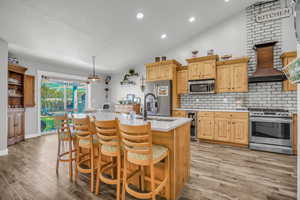 Kitchen with stainless steel appliances, vaulted ceiling, an island with sink, tasteful backsplash, and a kitchen bar