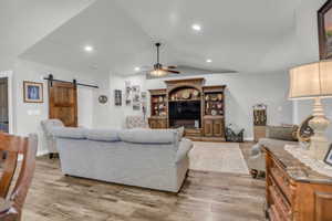 Living area with a barn door, a ceiling fan, wood finished floors, and recessed lighting