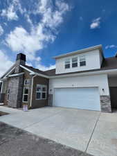 View of front of home with stone siding, stucco siding, concrete driveway, and a garage