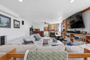 Living area with a stone fireplace, a ceiling fan, recessed lighting, and a textured ceiling
