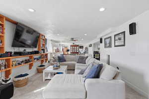 Living room featuring light carpet, recessed lighting, a ceiling fan, and a textured ceiling