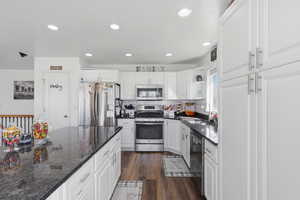 Kitchen featuring open shelves, stainless steel appliances, white cabinets, dark stone counters, and dark wood-style flooring