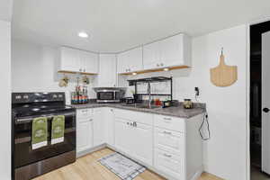 Kitchen featuring range with electric stovetop, dark countertops, white cabinetry, light wood-type flooring, and stainless steel microwave