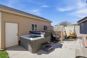 View of patio / terrace with a hot tub, a greenhouse, and an outbuilding
