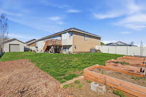 Rear view of property with a gate, a deck, a fenced backyard, a vegetable garden, and a garage