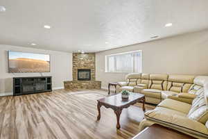 Living room with a fireplace, wood finished floors, a textured ceiling, and recessed lighting