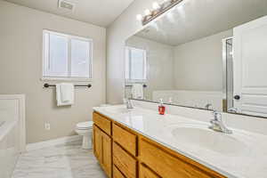 Full bath with double vanity, a garden tub, and light marble finish flooring