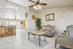 Sitting room with ceiling fan, an upstairs landing, lofted ceiling, and light marble finish flooring