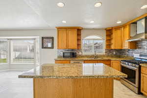 Kitchen featuring stainless steel appliances, light stone counters, decorative backsplash, a kitchen island, and recessed lighting