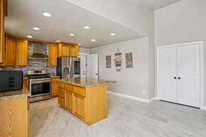 Kitchen featuring light marble finish floors, stainless steel appliances, light stone counters, a kitchen island, and recessed lighting
