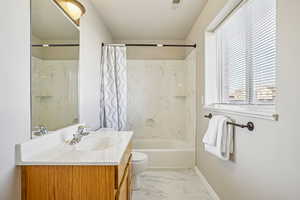 Full bath featuring vanity, shower / bath combo with shower curtain, and light marble finish floors