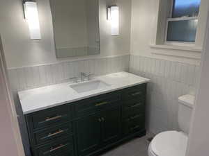 Half bathroom featuring vanity, a wainscoted wall, and light tile patterned flooring