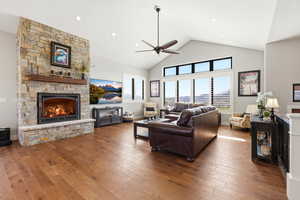 Living area featuring a stone fireplace, a high ceiling, hardwood / wood-style flooring, and a ceiling fan