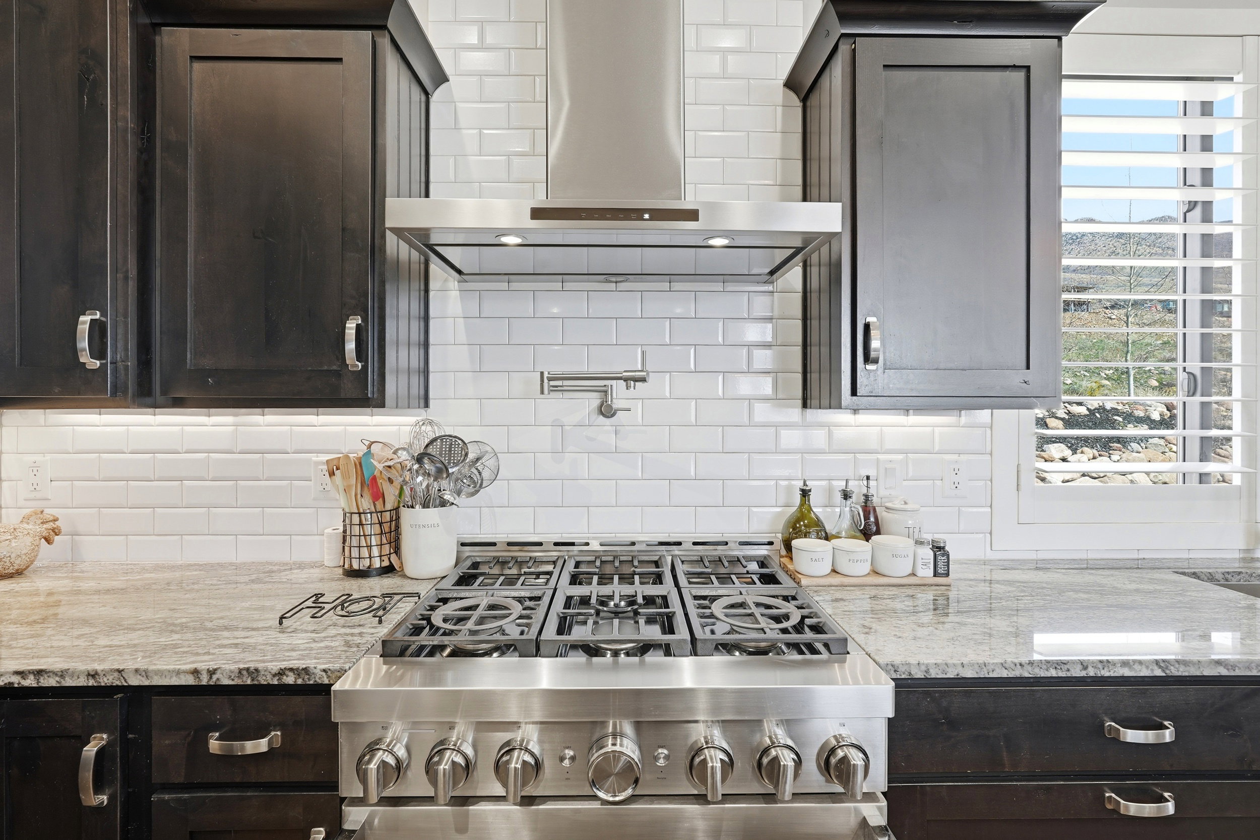 Kitchen with dark wood finish cabinets, light stone counters, gas stove, and backsplash