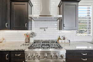 Kitchen with dark wood finish cabinets, light stone counters, gas stove, and backsplash