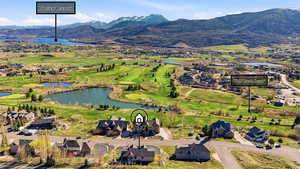 Aerial view of property and surrounding area with a water and mountain view, a local golf course, and nearby suburban area