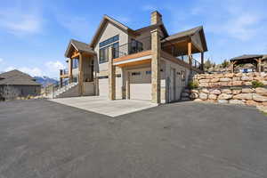 View of side of home with asphalt driveway, an attached garage, stone siding, a mountain view, and a chimney