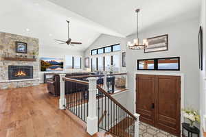 Entrance foyer with ceiling fan, a stone fireplace, vaulted ceiling, light wood finished floors, and suspended lighting