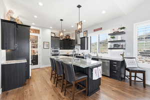 Kitchen with dark cabinetry, a kitchen breakfast bar, light stone counters, decorative backsplash, and an island with sink