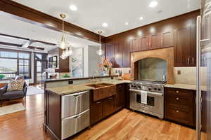 Kitchen featuring light stone counters, a peninsula, open floor plan, premium appliances, and light wood-style floors