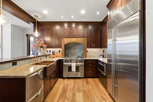 Kitchen featuring a peninsula, light stone countertops, high quality appliances, and dark wood finish cabinets