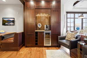 Indoor dry bar with light wood-type flooring, beverage cooler, recessed lighting, and light stone countertops