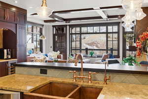 Kitchen with beverage cooler, coffered ceiling, open floor plan, healthy amount of natural light, and light stone countertops