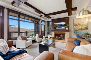 Living room with a lit fireplace, coffered ceiling, and healthy amount of natural light