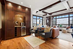 Living area featuring coffered ceiling, light wood-style floors, beverage cooler, and a dry bar