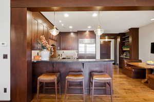 Kitchen with dark countertops, a kitchen breakfast bar, a peninsula, stainless steel built in fridge, and light wood finished floors