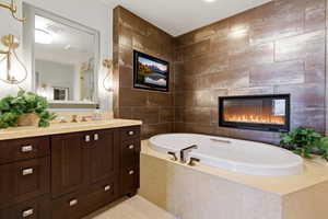 Full bath with vanity, a tile fireplace, a bath, light tile patterned floors, and tile walls