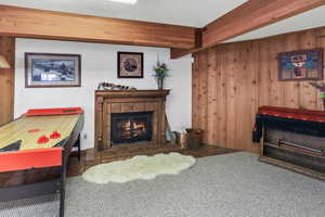 Living area with a tiled fireplace, wooden walls, and carpet