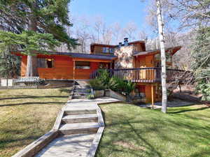 View of property featuring a patio area, a chimney, lawnarea, and a wooden deck
