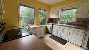 Kitchen featuring electric range, stainless steel dishwasher, white cabinetry, backsplash, and light tile patterned flooring