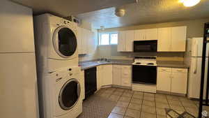 Kitchen featuring black appliances, white cabinetry, a textured ceiling, light tile patterned flooring, and stacked washer and clothes dryer
