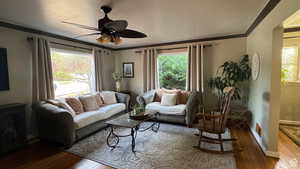 Living room with wood finished floors, ornamental molding, plenty of natural light, and a ceiling fan