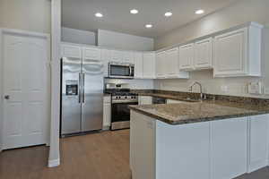 Kitchen featuring white cabinets, a peninsula, stainless steel appliances, dark stone countertops, and recessed lighting